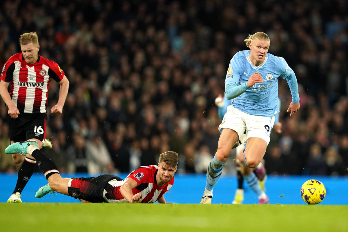 Manchester City striker Erling Haaland pictured (right) running with the ball following a slip  by Brentford defender Kristoffer Ajer (center) during a Premier League game at the Etihad Stadium in February 2024