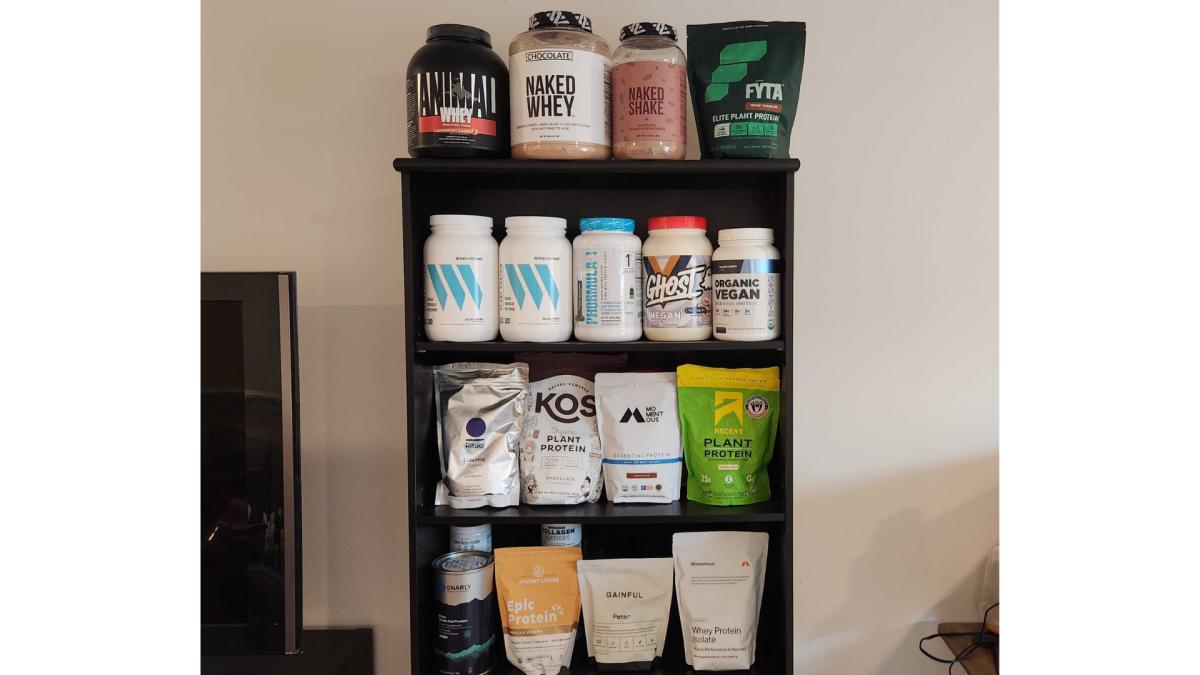 A four-shelf bookcase filled with various containers of protein powder.