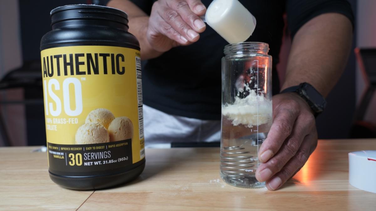 A man scooping Jacked Factory ISO whey protein powder into a shaker bottle half full of water