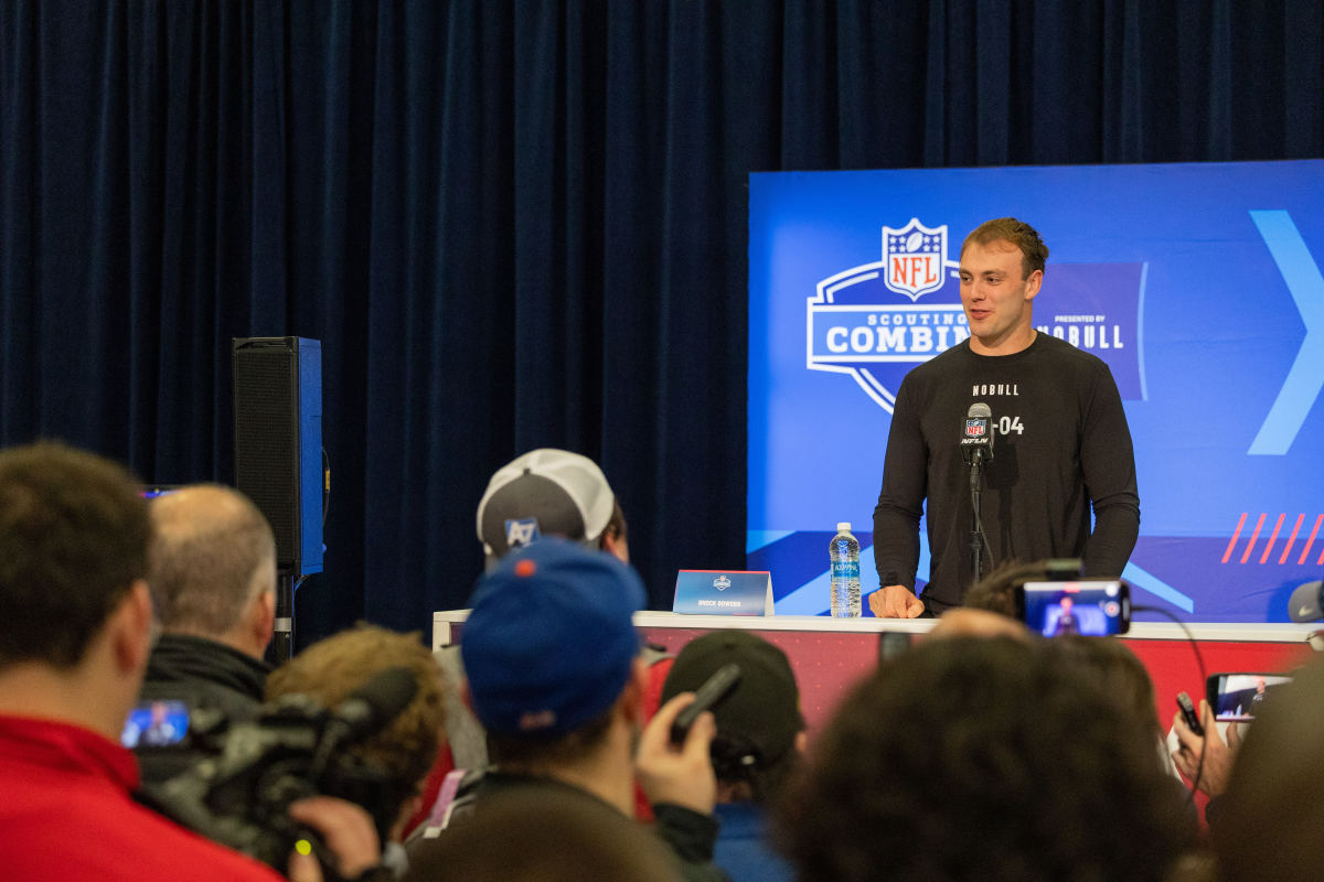 Brock Bowers stands at a podium in front of a microphone at the NFL scouting combine