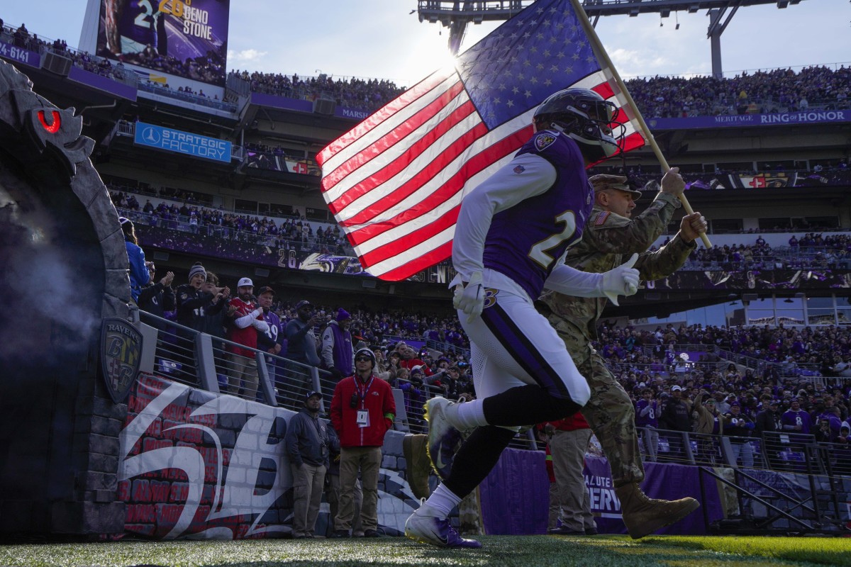 Nov 12, 2023; Baltimore, Maryland, USA; Baltimore Ravens safety Geno Stone (26) takes the field with a military service member before a game against the Cleveland Browns at M&T Bank Stadium.