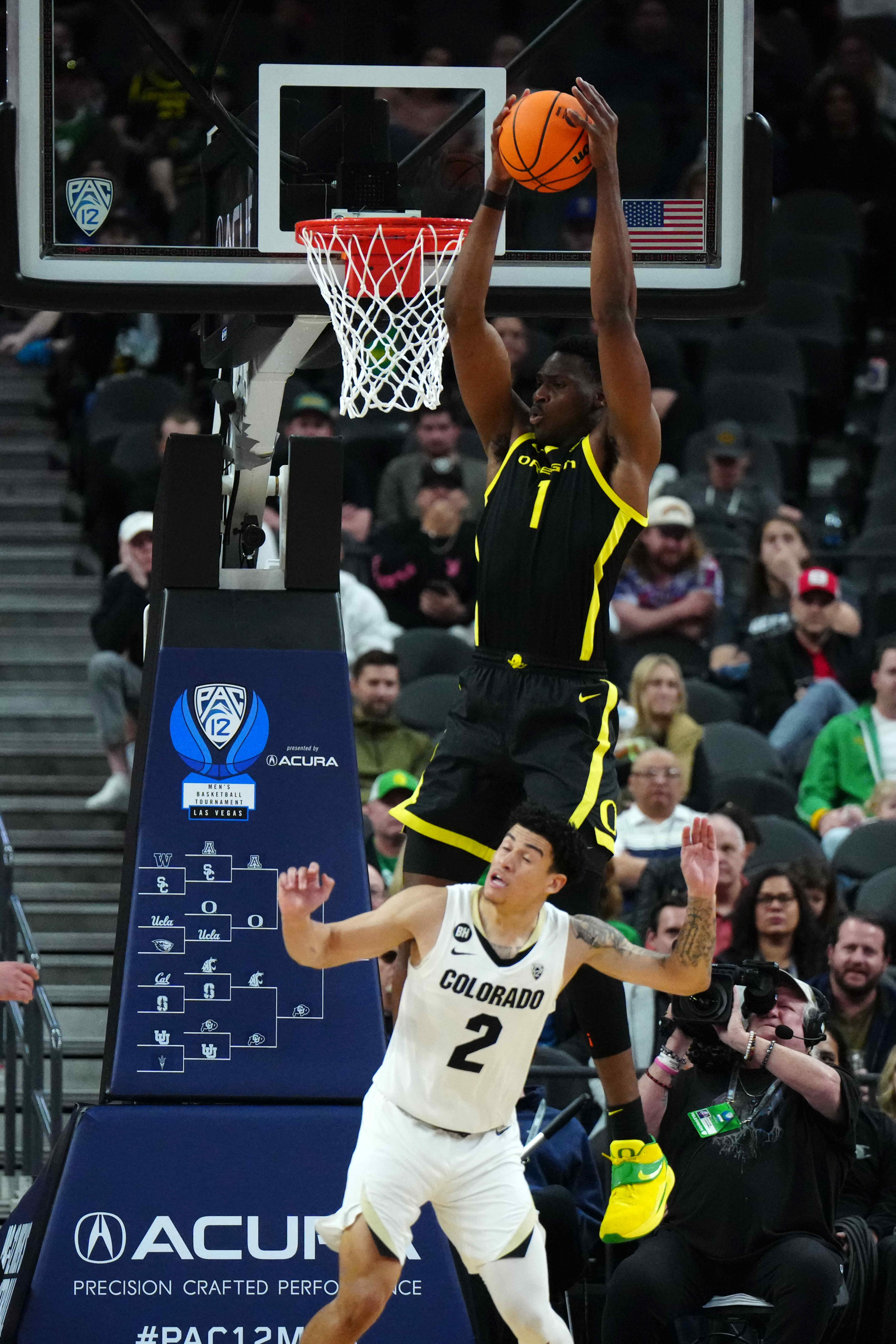 Oregon Ducks center N'Faly flies over a Colorado Buffaloes defender for a dunk in the 2024 Pac-12 Tournament.