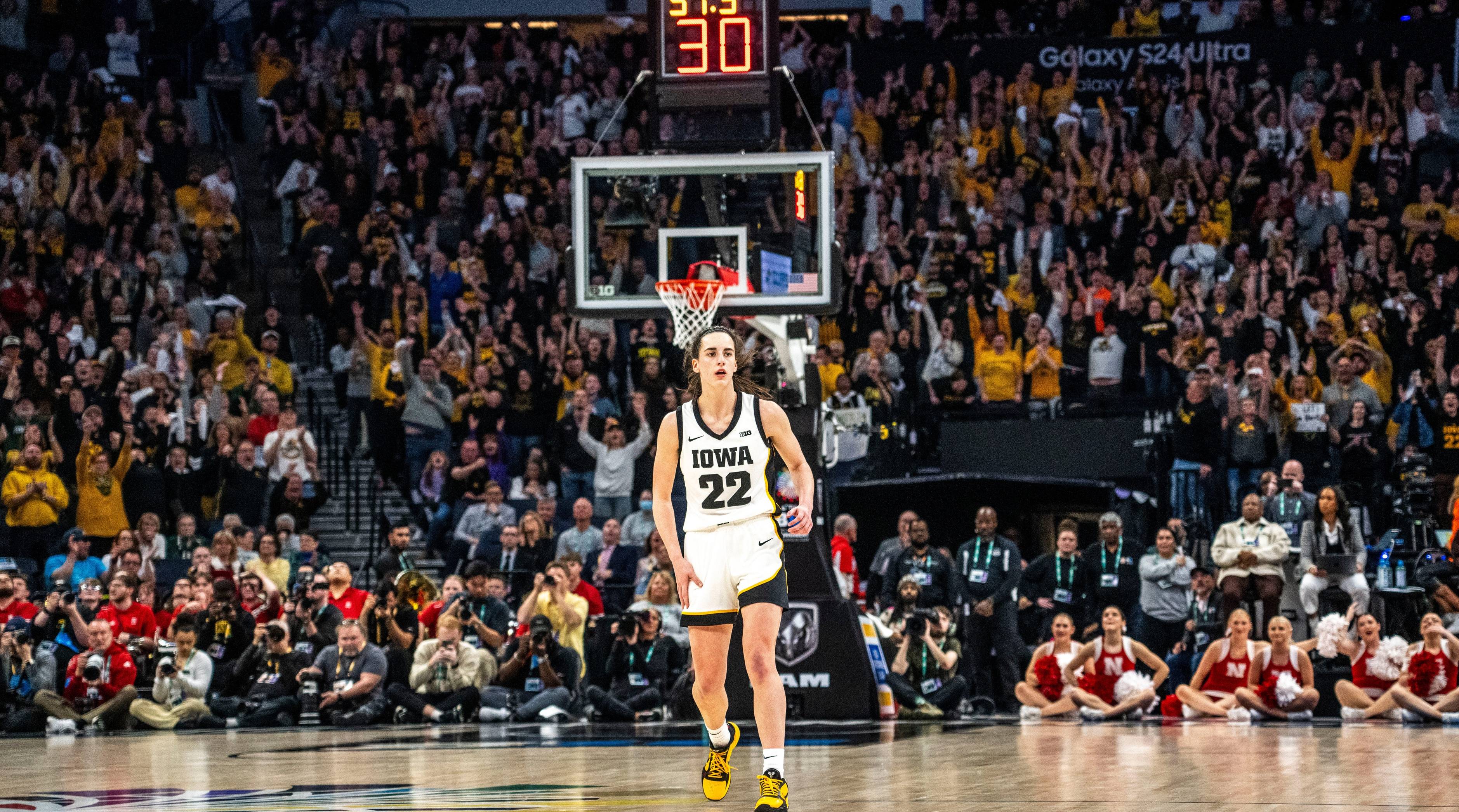 Caitlin Clark looks on from midcourt in front of a crowd during a game.