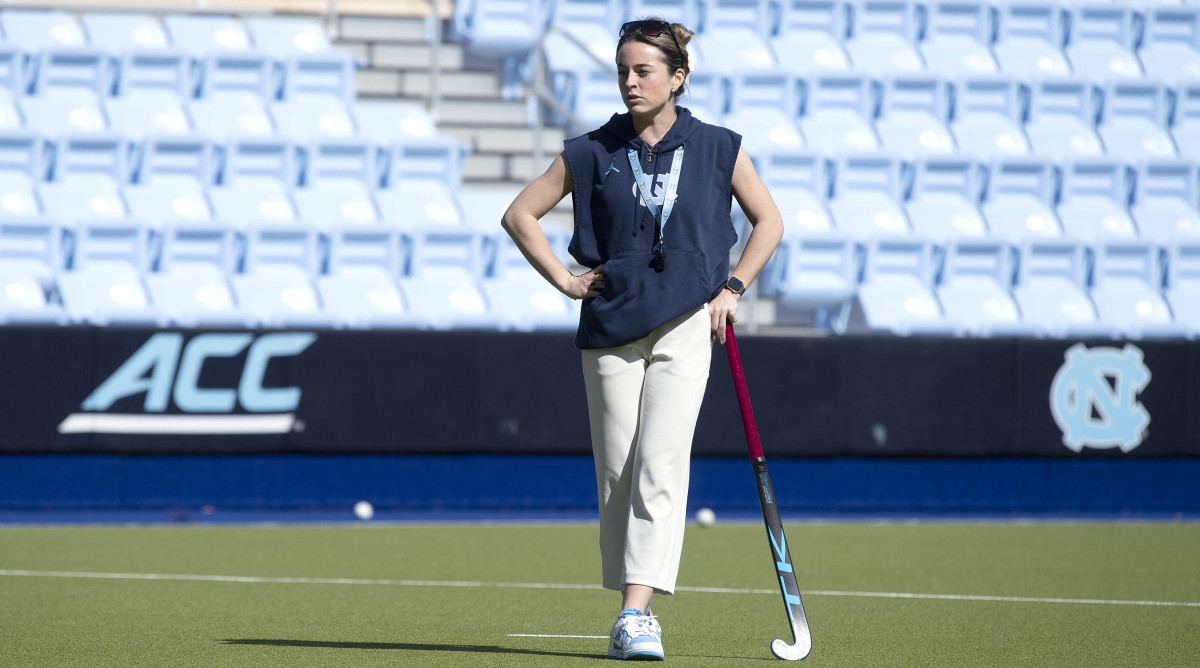 UNC field hockey coach Erin Matson stands with a field hockey stick while watching her team practice.