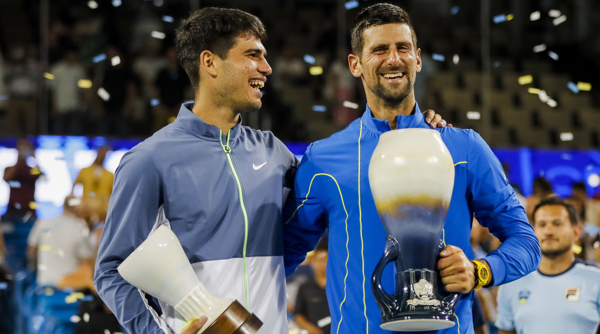 Carlos Alcaraz and Novak Djokovic stand side by side holding their trophies after the the men's final of the Western and Southern Open tennis tournament.