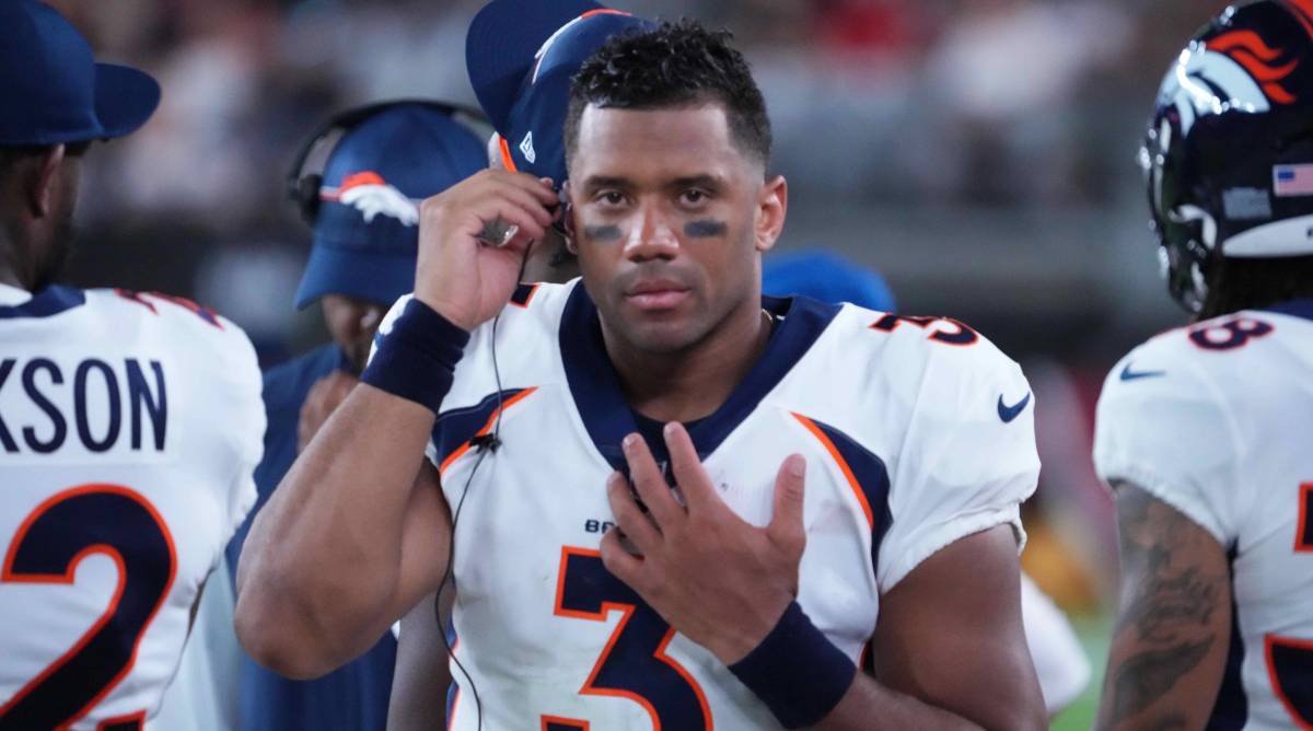 Broncos quarterback listens to a headset while standing on the sideline during a game.