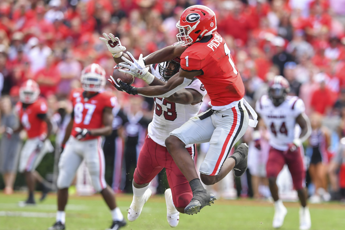 Wearing a Georgia Bulldogs uniform, George Pickens jumps to try to catch a ball as a South Carolina defender tries to block it