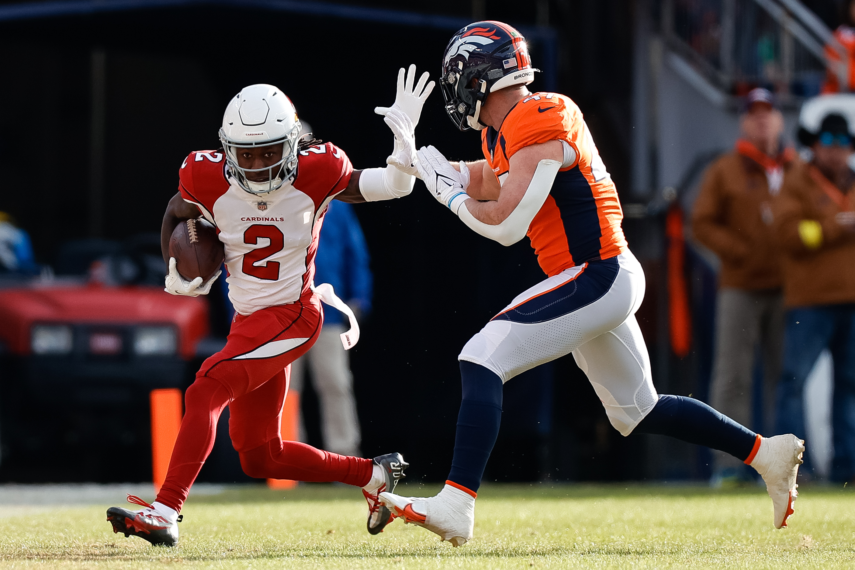 Marquise Brown runs with one hand up and one hand holding the ball to try to block a Broncos defender
