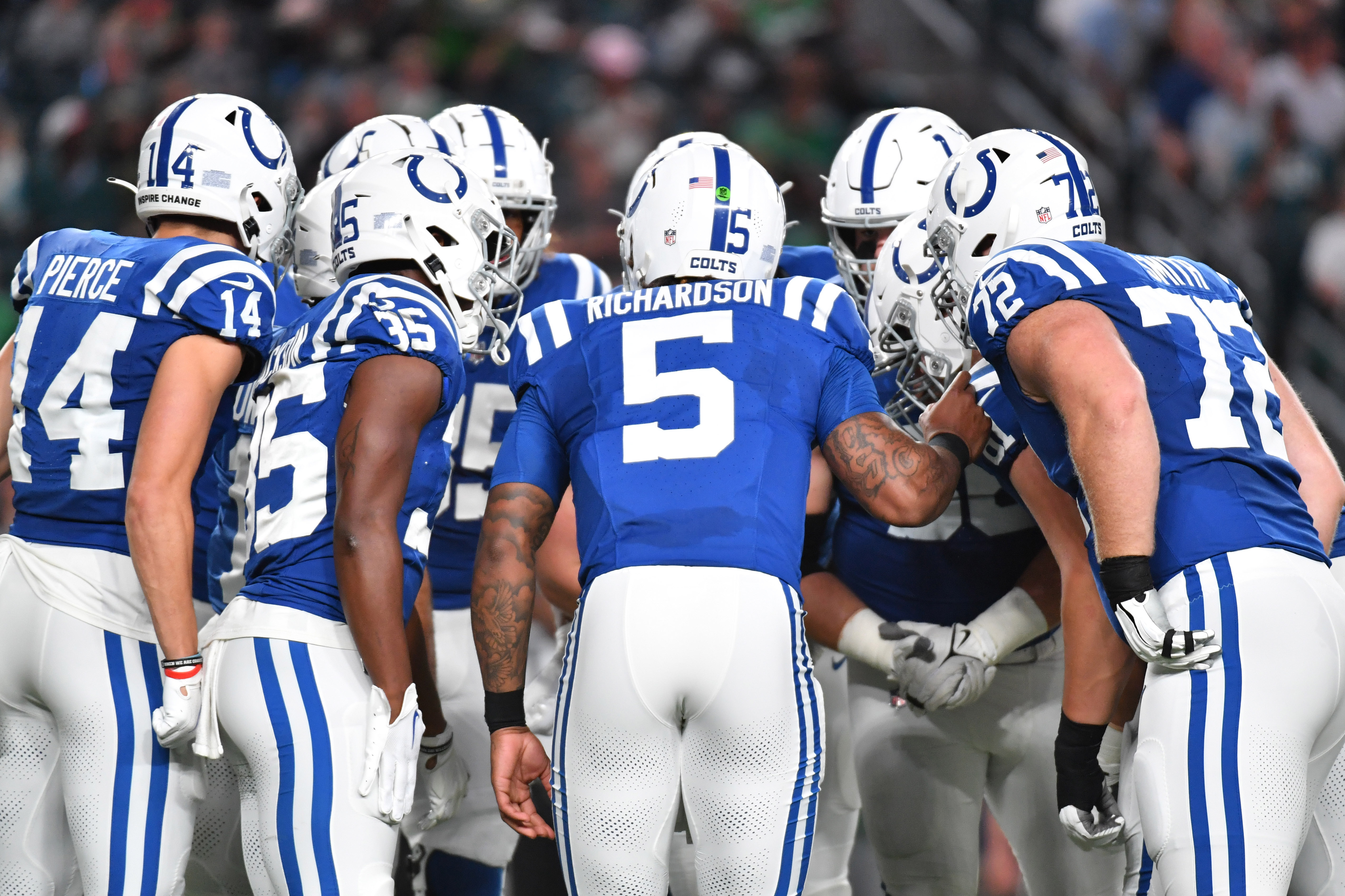 A huddle of Colts players lean in with their heads toward the center, with Anthony Richardson in the middle and his name printed across the back of his jersey
