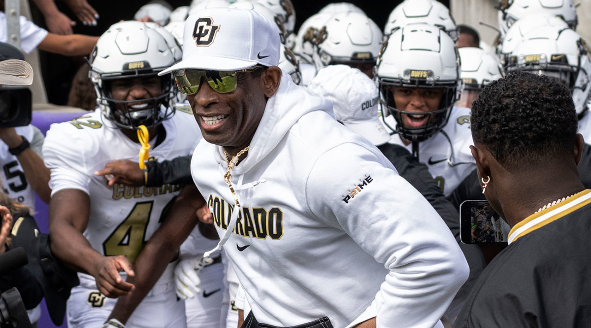 Deion Sanders smiling with players behind him during his first game coaching Colorado