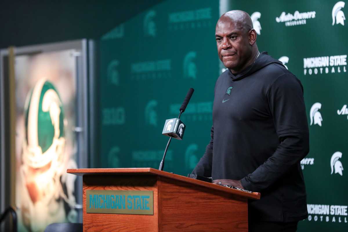 Mel Tucker stands behind a Michigan State branded podium with a microphone attatched