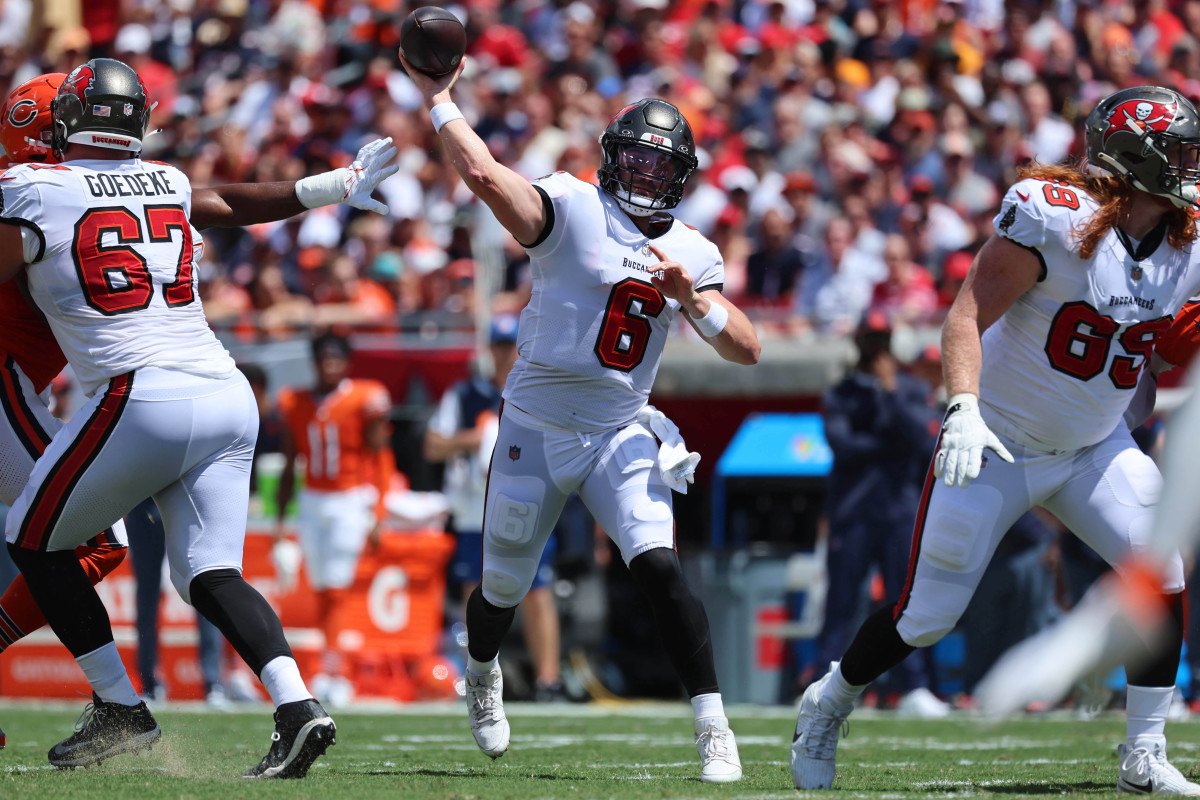 Baker Mayfield steps and throws the football, and two offensive linemen block on either side