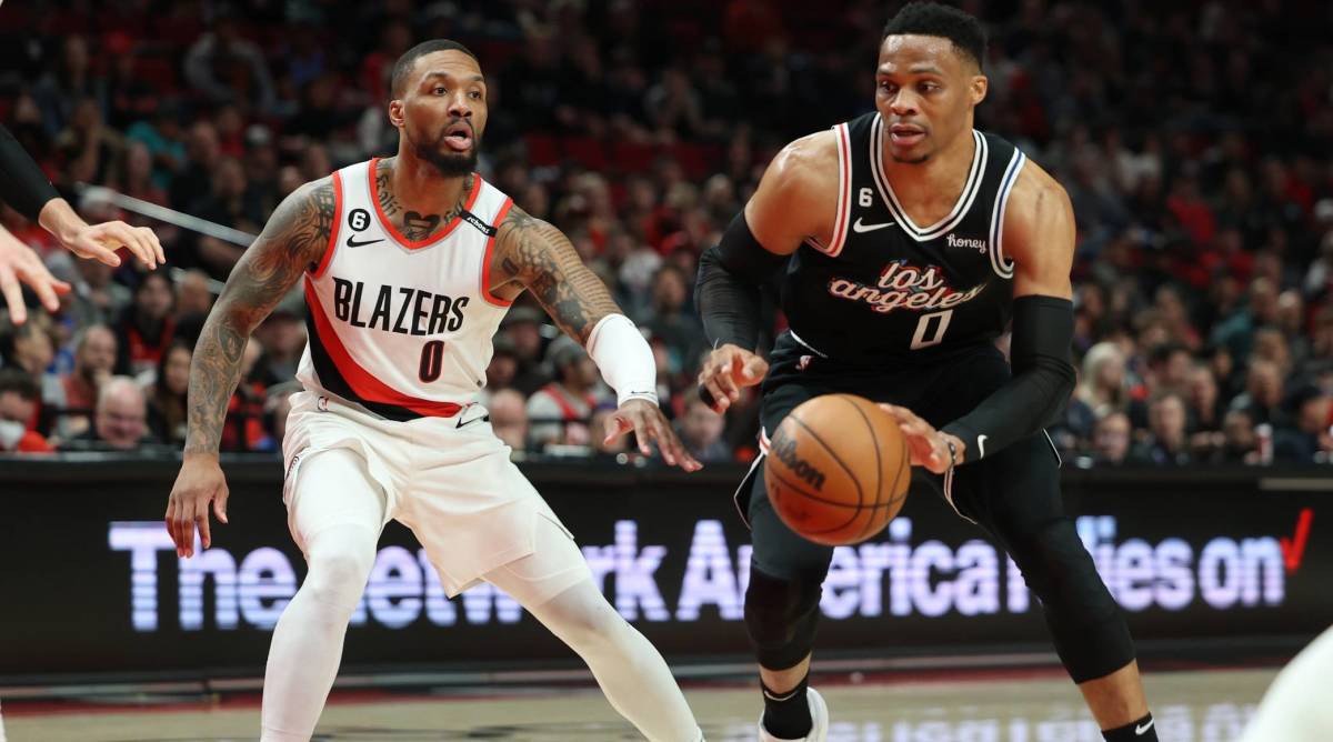 Clippers point guard Russell Westbrook dribbles a ball while being defended by Blazers point guard Damian Lillard in a game.