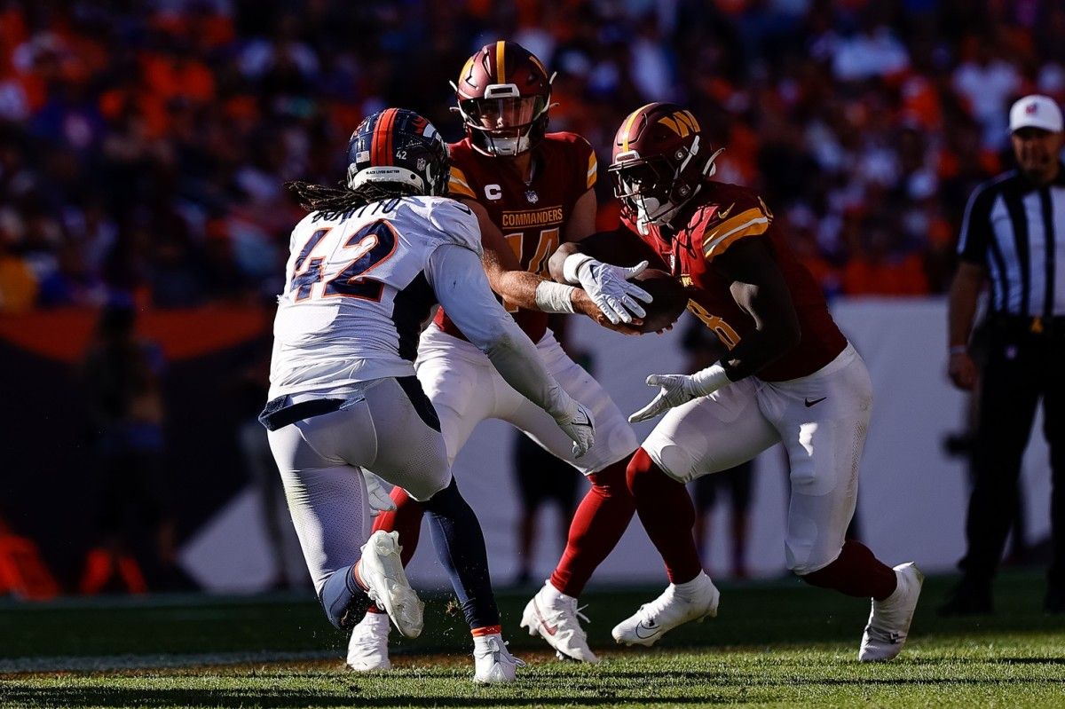 Washington Commanders quarterback Sam Howell (14) hands the ball off to running back Brian Robinson Jr. (8) as Denver Broncos linebacker Nik Bonitto (42) rushes in the third quarter at Empower Field at Mile High.