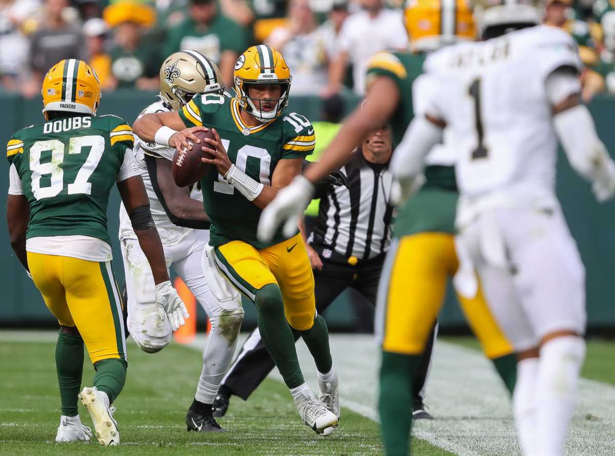 Jordan Love runs with the ball in two hands as a Saints player chases him