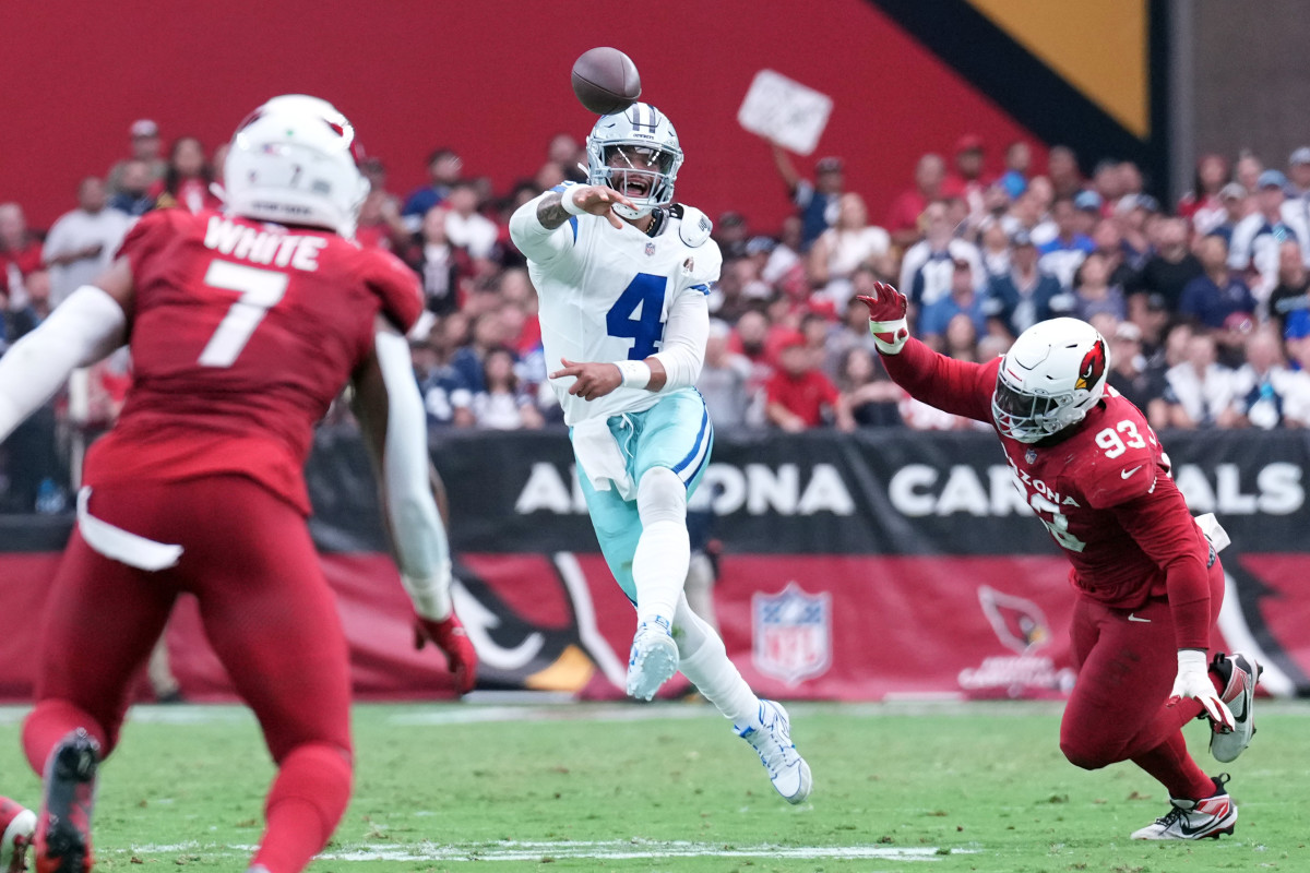 Dak Prescott throws the ball as one foot comes off the ground and a Cardinals player lunges toward him