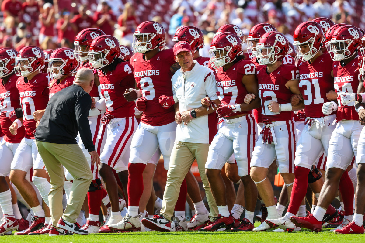 Brent Venables and the Oklahoma football team walk in a group with their arms linked
