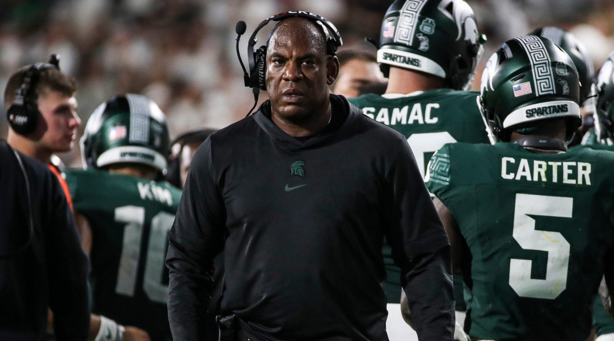 Mel Tucker wears a headset standing in front of a group of Michigan State players