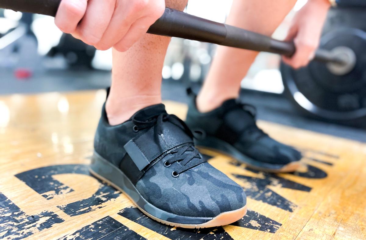 closeup of person lifting barbell wearing NoBull Canvas lifters in camo colorway on wood platform
