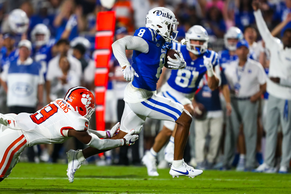 A Duke football player running with the ball while a Clemson player tries to tackle him.
