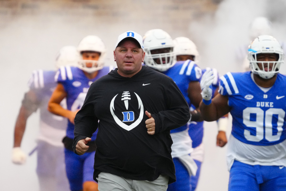 Coach Mike Elko running with Duke football players behind him