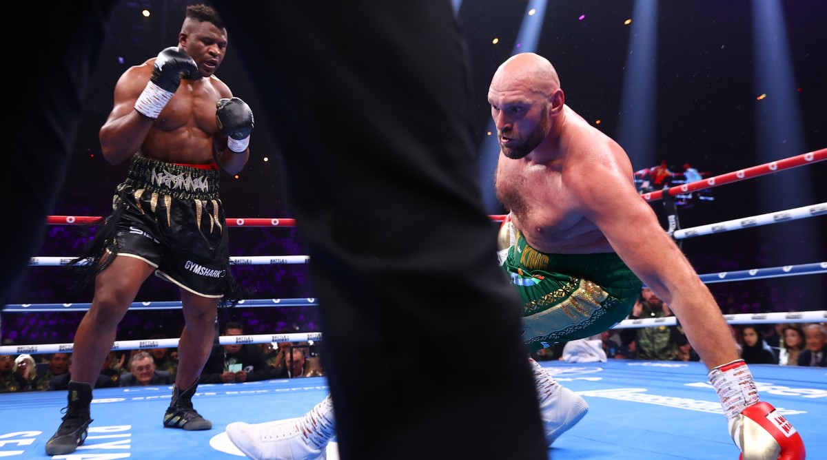 Tyson Fury falls to the ground after taking a punch from Francis Ngannou during a boxing match.