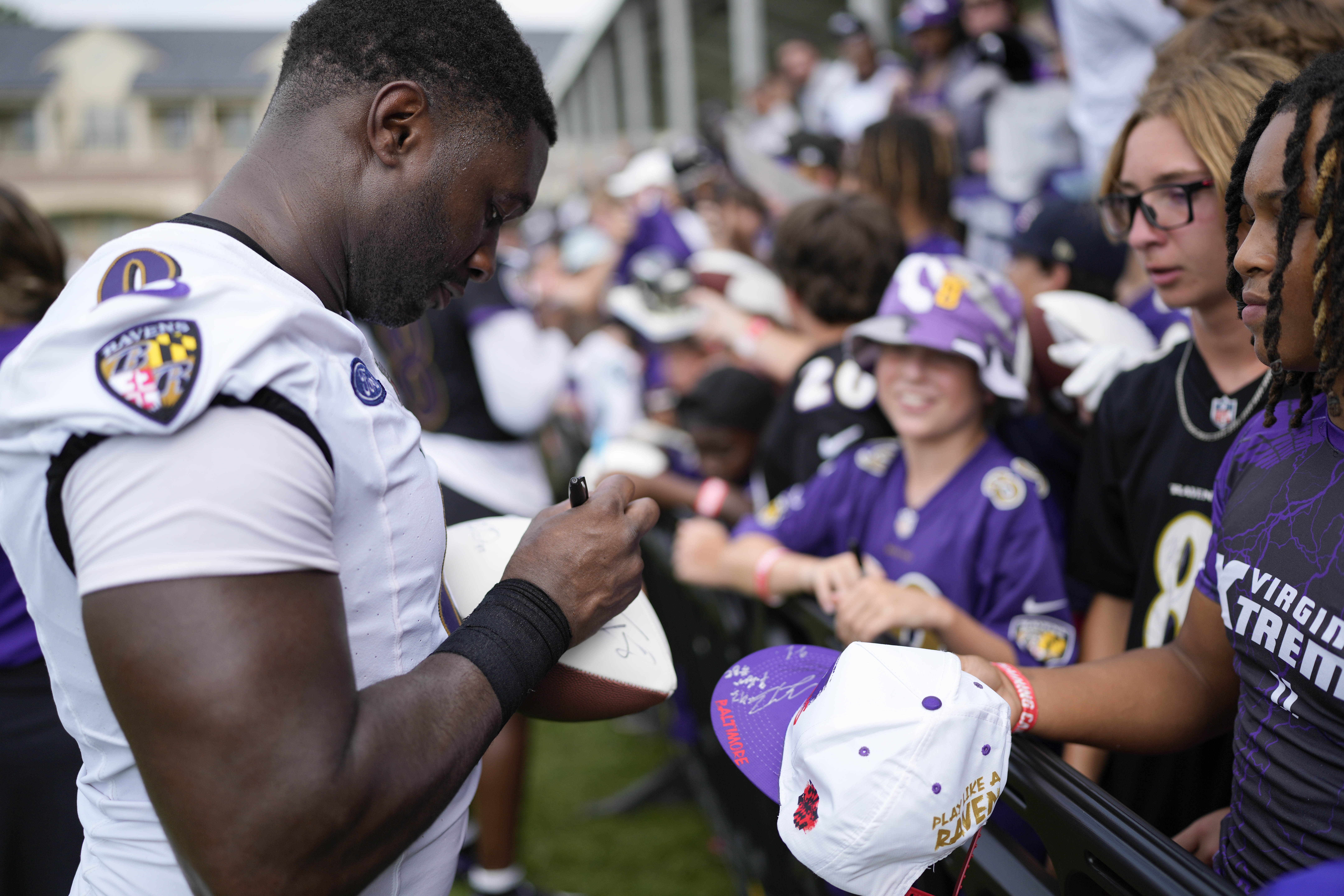 Roquan Smith autographs a small football as a crowd of kids stand behind the fence in front of him