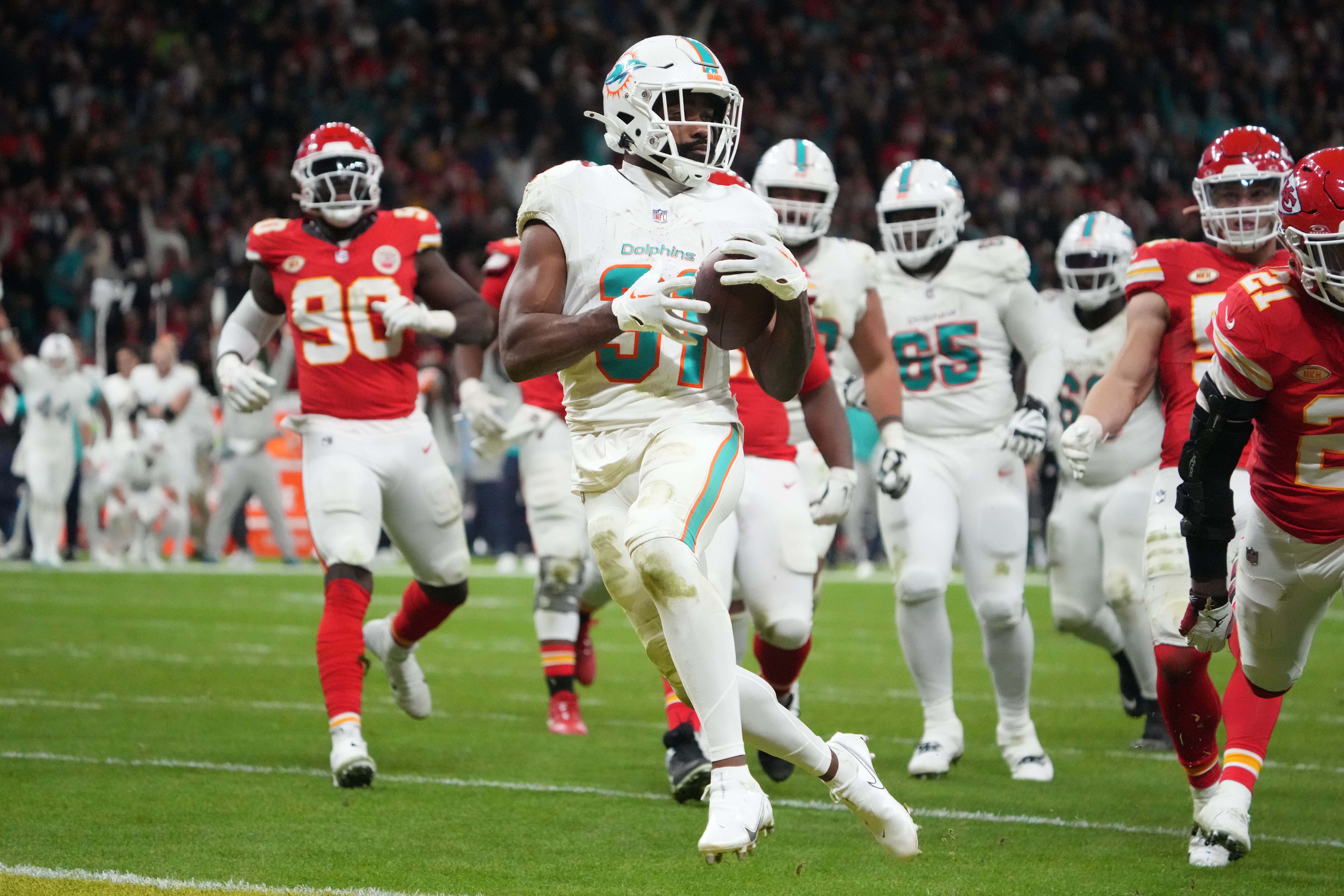 Miami Dolphins running back Raheem Mostert carries the ball in his hands as he runs while a slew of Chiefs players run behind him