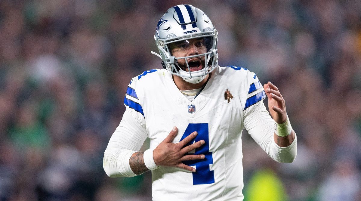Dak Prescott reaches a hand out and grabs his chest with the other reacting to a play