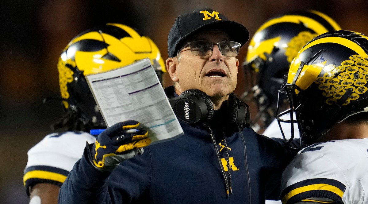 Michigan coach Jim Harbaugh motions while standing on the sideline among his players.