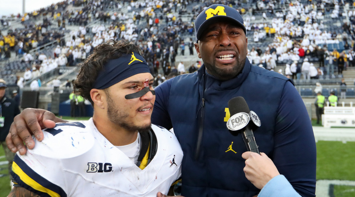 Wolverines offensive line coach Sherrone Moore, right, does an interview through tears as running back Blake Corum, left, looks on.