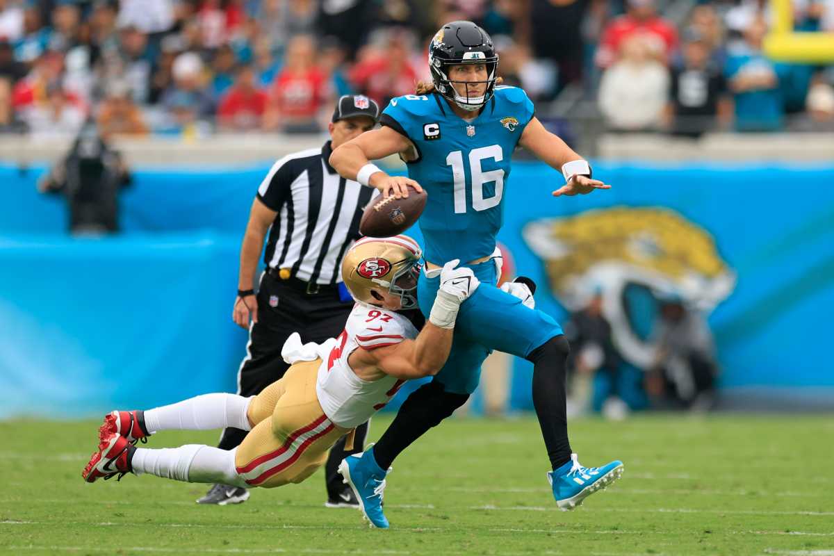Trevor Lawrence runs with the ball in one hand as a 49ers defender grabs his waist to tackle him