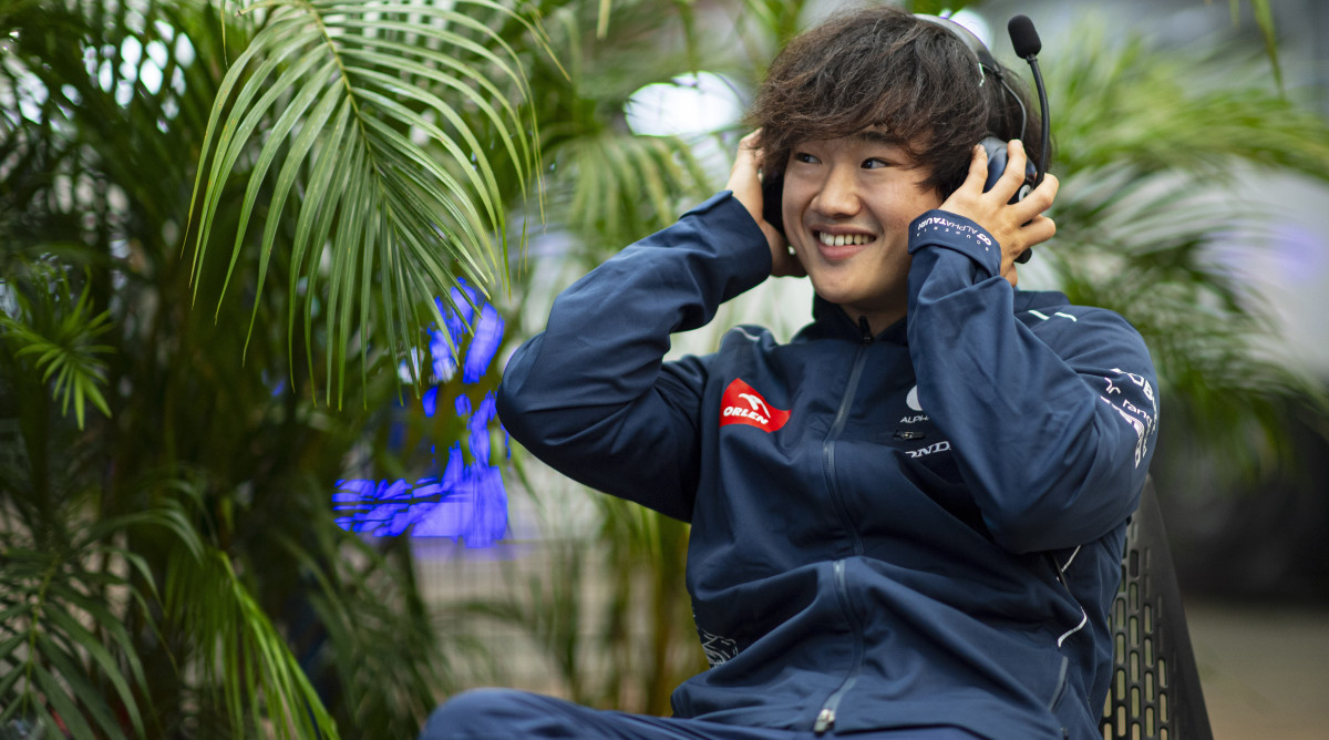 AlphaTauri driver Yuki Tsunoda smiles during an interview while wearing a headset.