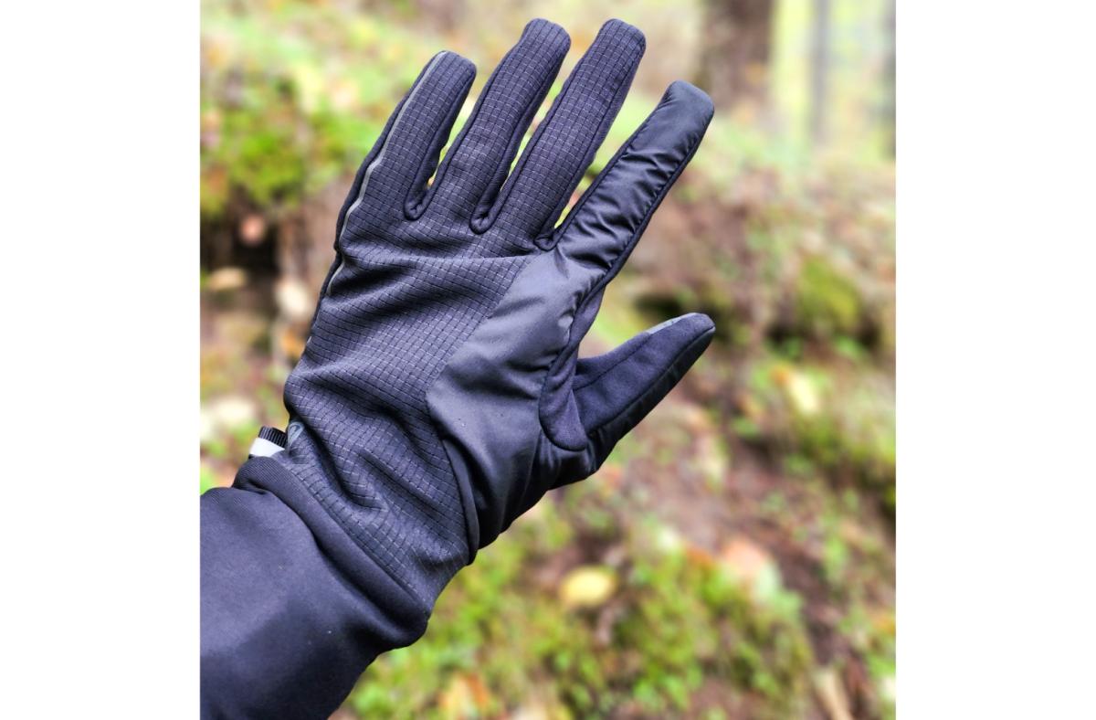 A hand wearing a black lululemon running glove outside in a forest setting
