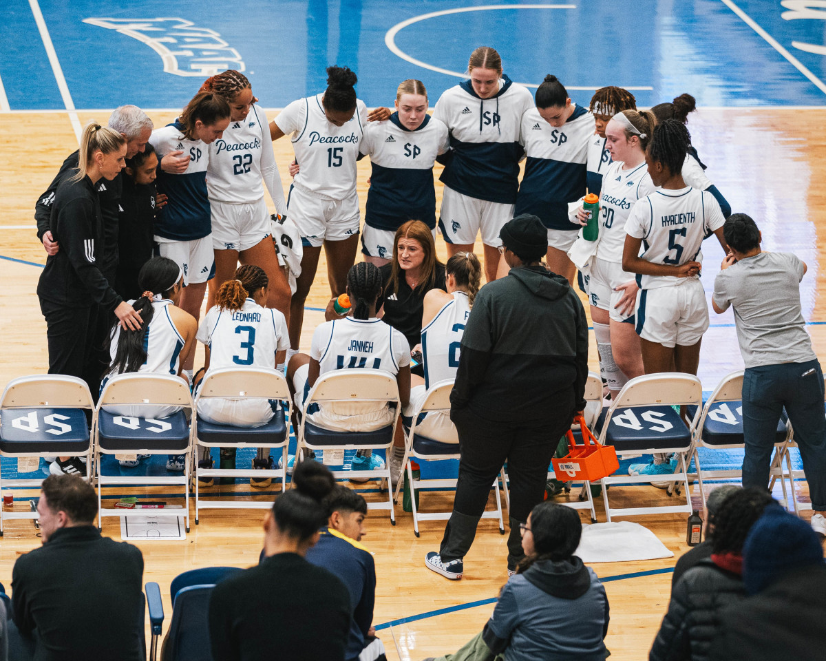 Saint Peter’s women’s basketball coach Jennifer Leedham addresses her team in a huddle around the bench.