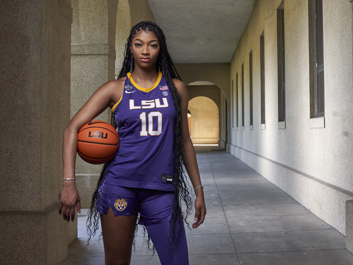 LSU star basketball player Angel Reese poses in uniform with a basketball on her hip.