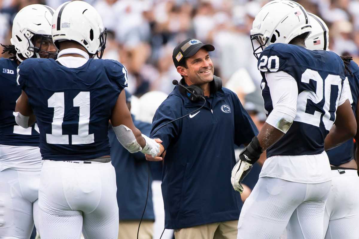 Manny Diaz reaches out to shake a players hand as he smiles at a group of Penn State players who come to the sideline