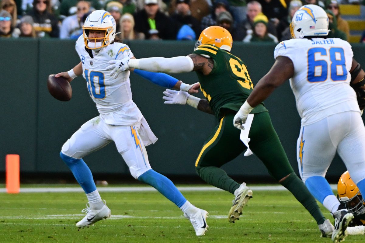 Justin Herbert runs with the ball in one hand while a Packers defender reaches for him
