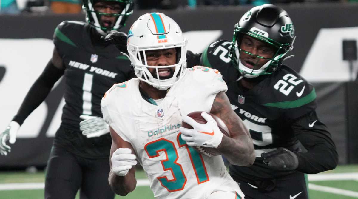 Dolphins running back Raheem Mostert, center, is pursued by Jets defenders Sauce Gardner and Tony Adams