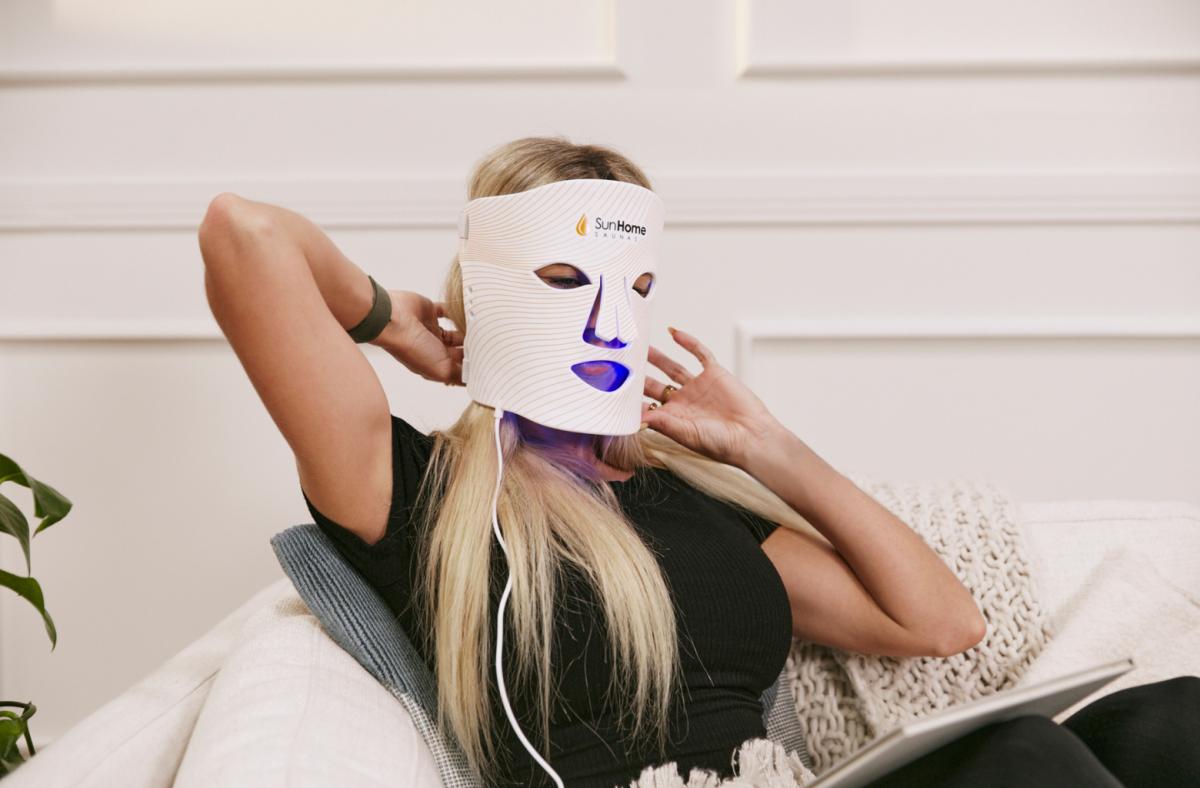 Women holding LED face mask on face.