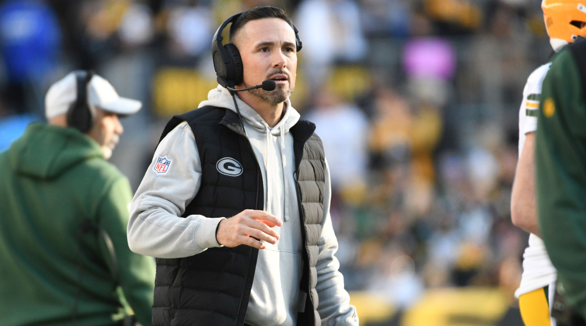 Matt LaFleur puts one hand up as he walks with a headset on