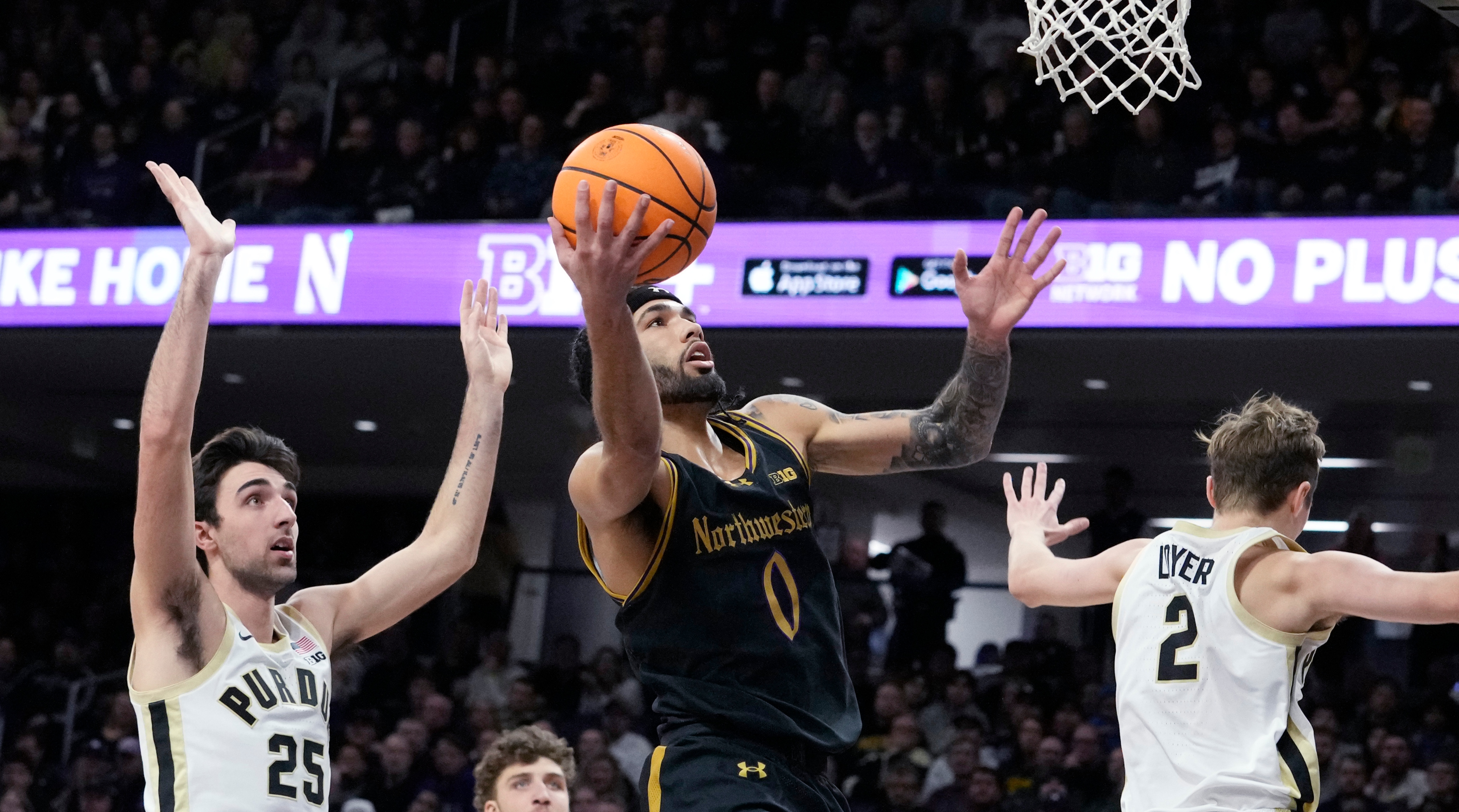 Northwestern point guard Boo Buie drives to the basket for a layup between two Purdue defenders.