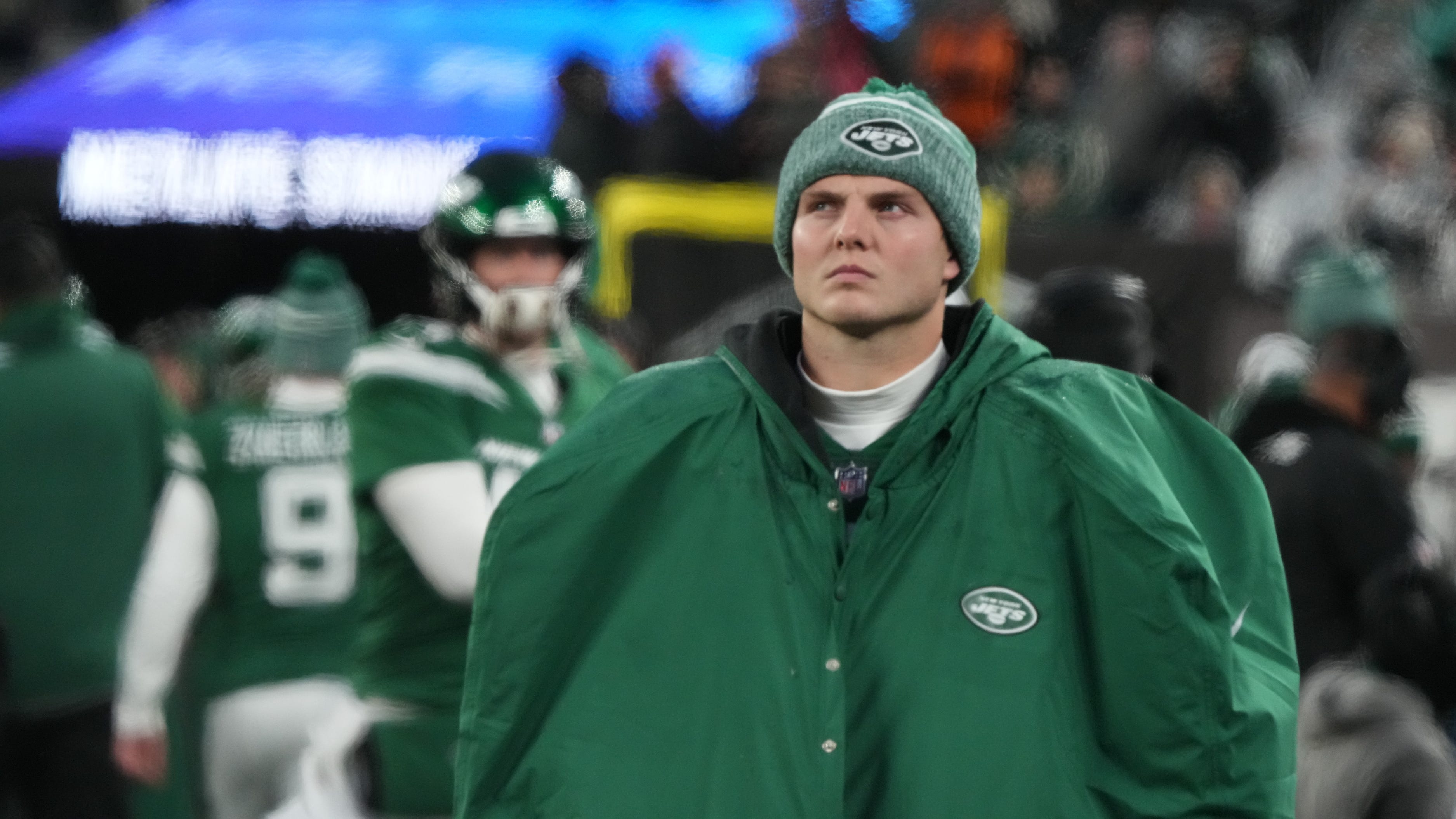 Zach Wilson stands looking up wearing a big green Jets jacket