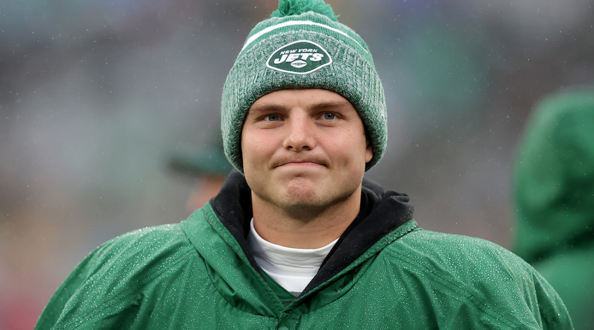 Zach Wilson smirks contentedly while wearing a warm jacket and hat on the sideline during a Jets win