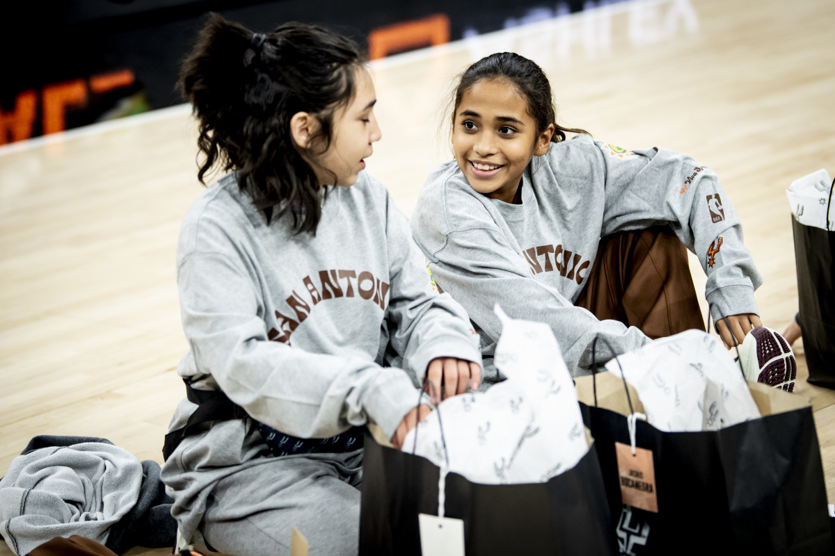 Two girls from S.J. Davis Middle School unwrap their gifts from the San Antonio Spurs at Frost Bank Center. Each bag was labeled with the girls' names and given to them by their coaches and the Coyote.