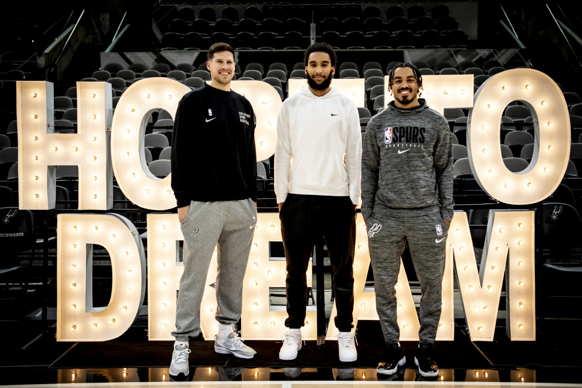 San Antonio Spurs forwards Doug McDermott, Julian Champagnie and point guard Tre Jones stand in front of the light-up "Hope to Dream" event sign following a skills clinic with S.J. Davis Middle School.