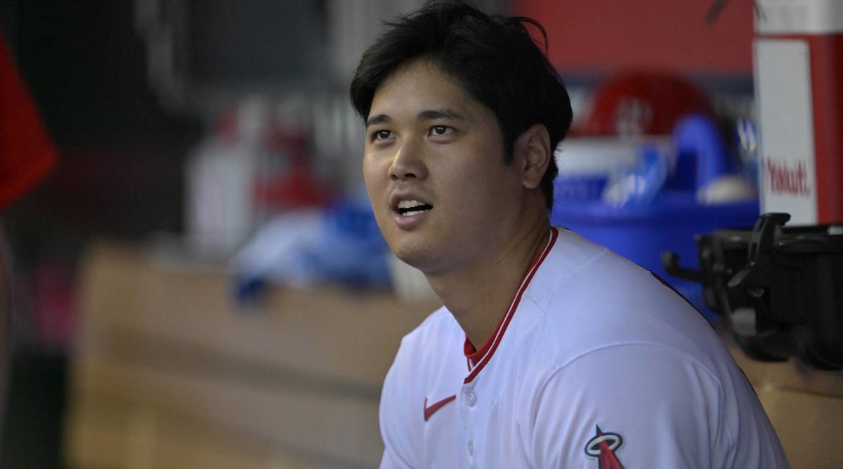 Angels star Shohei Ohtani looks up while speaking to someone in the dugout of a game.