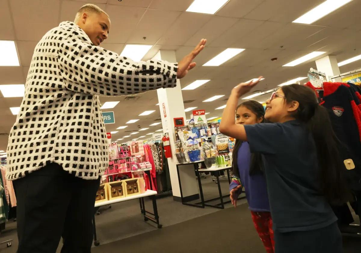 Customers Jhoanna Castro, 10, center, and Evelyn Chimbay, 7, get a high-five from New England Patriots tight end Pharaoh Brown at a surprise holiday payoff event at Brockton Citi Trends on Tuesday, Dec. 12, 2023. 