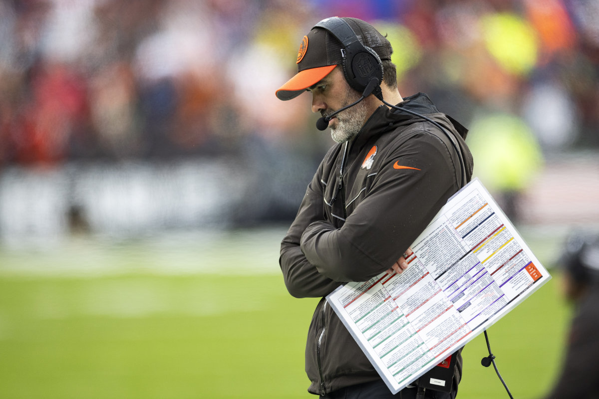 Kevin Stefanski looks down wearing a headset and holding a laminated play sheet under his arm