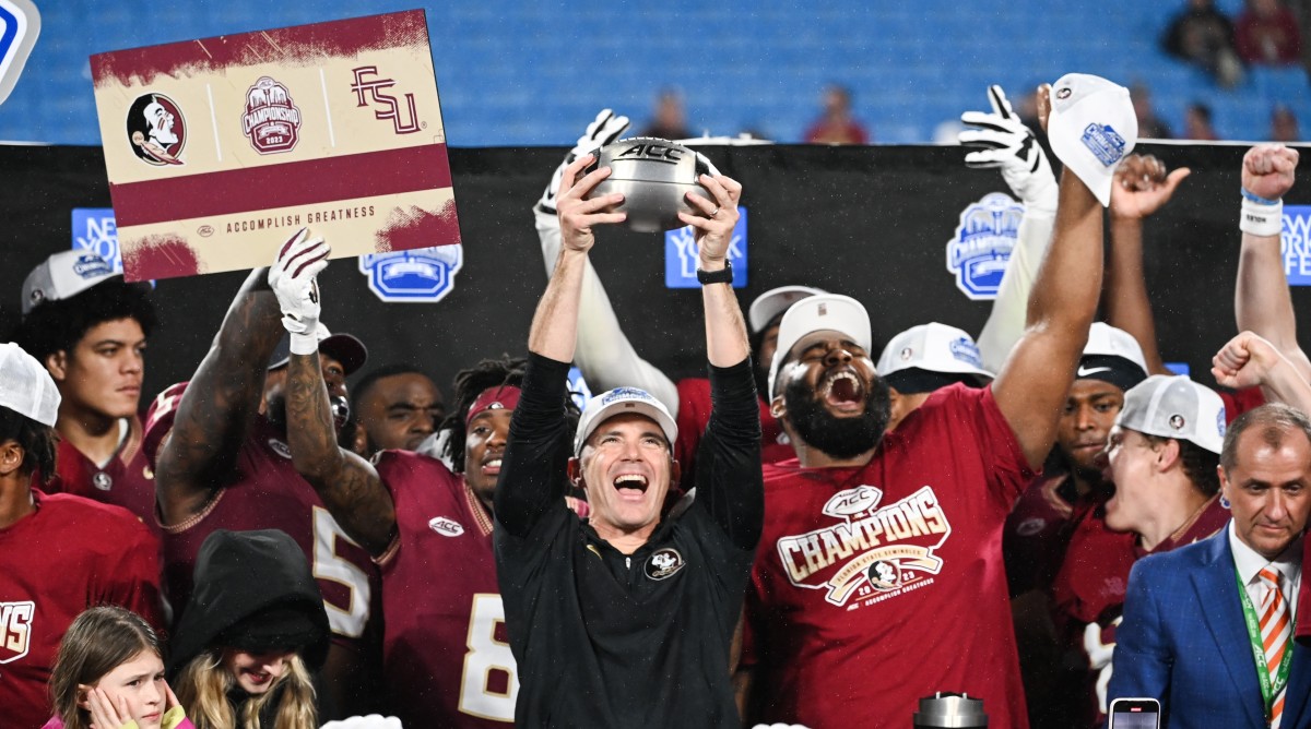 Florida State football coach Mike Norvell hoists up the ACC championship trophy while standing alongside his team.